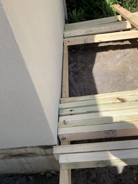 Ledger board spaced off house wall with packers for drainage on Little Bay deck build