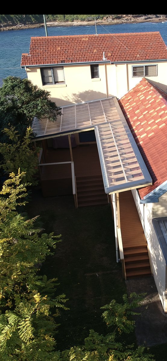 Aerial view of an L-shaped polycarbonate pergola over a multi-level deck on a coastal property